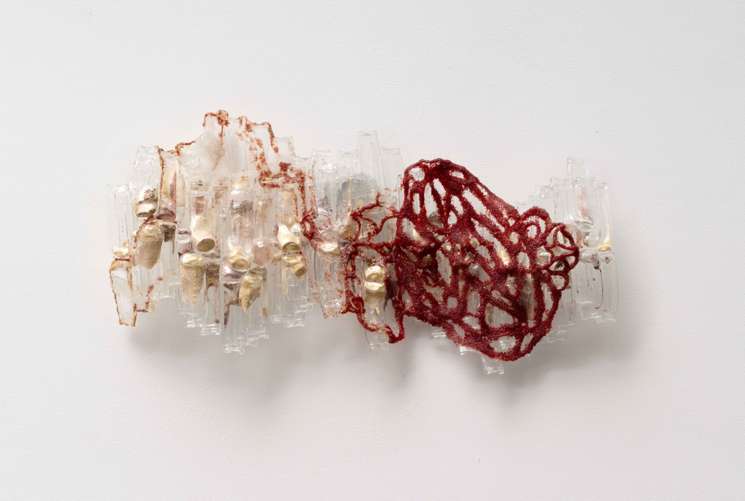 glass wall sculpture of curved bottles covered in a red lace net shape