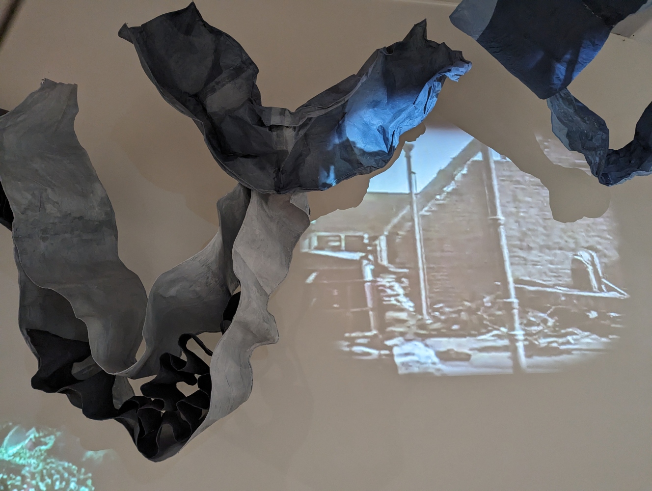 gray sculptural paper forms draped in front of video of buildings