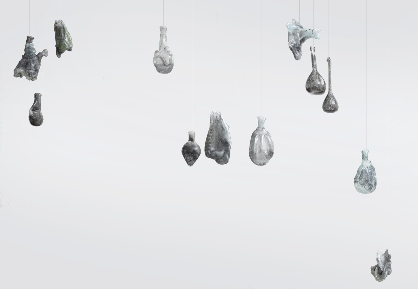 Installation of 16 suspended melted bottles with black designs on the interior